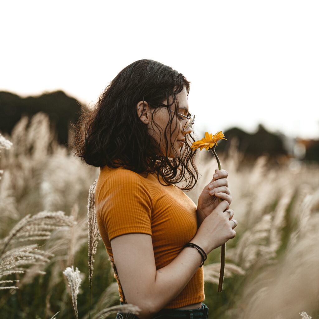 Jeune femme sentant une fleur, les yeux fermés. Image pour introduire la règle N°1 J'évite de stresser.